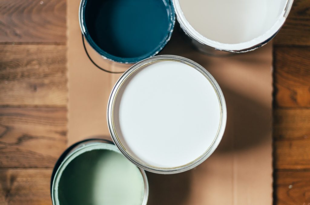 Paint cans during house renovation, process of choosing paint for the walls, different colors of white, green and blue on wooden floor